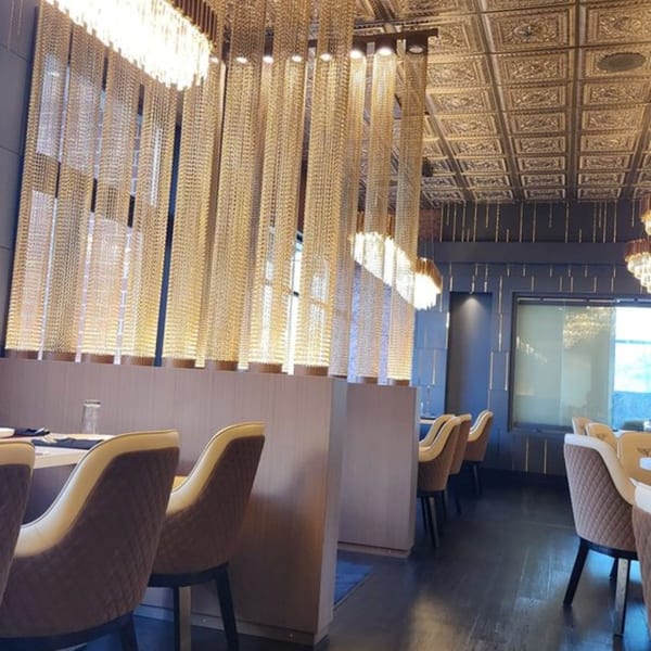 Elegant restaurant interior with gold chain curtains, ornate ceiling, and plush chairs at set tables.