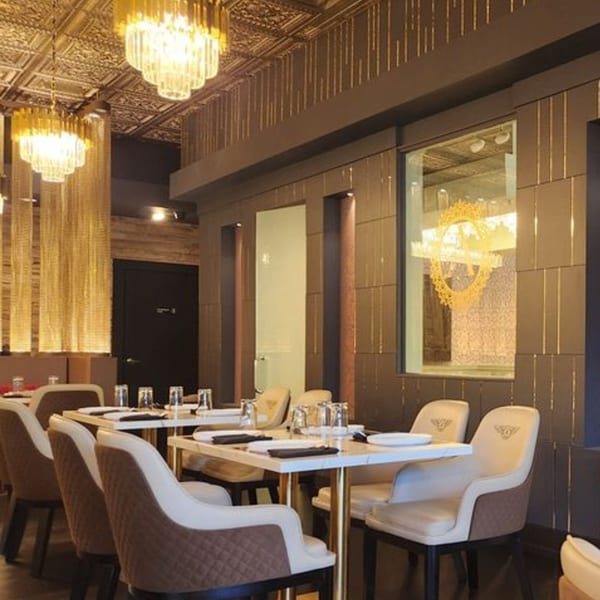 Elegant restaurant interior with gold chandeliers, patterned ceiling, and set tables with plush chairs.