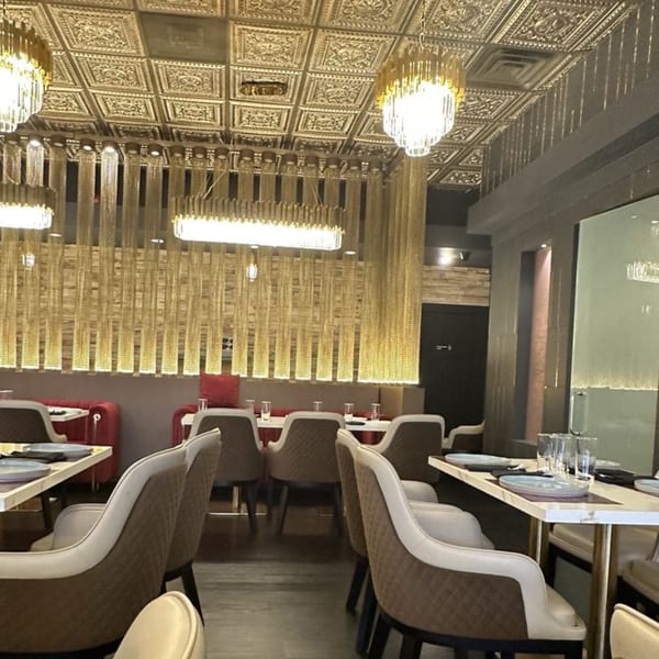 Elegant restaurant interior with gold chain curtains, ornate ceiling, and modern dining tables with chairs.