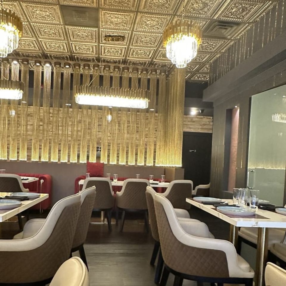 Elegant restaurant interior with gold chain curtains, ornate ceiling, and modern dining tables with chairs.